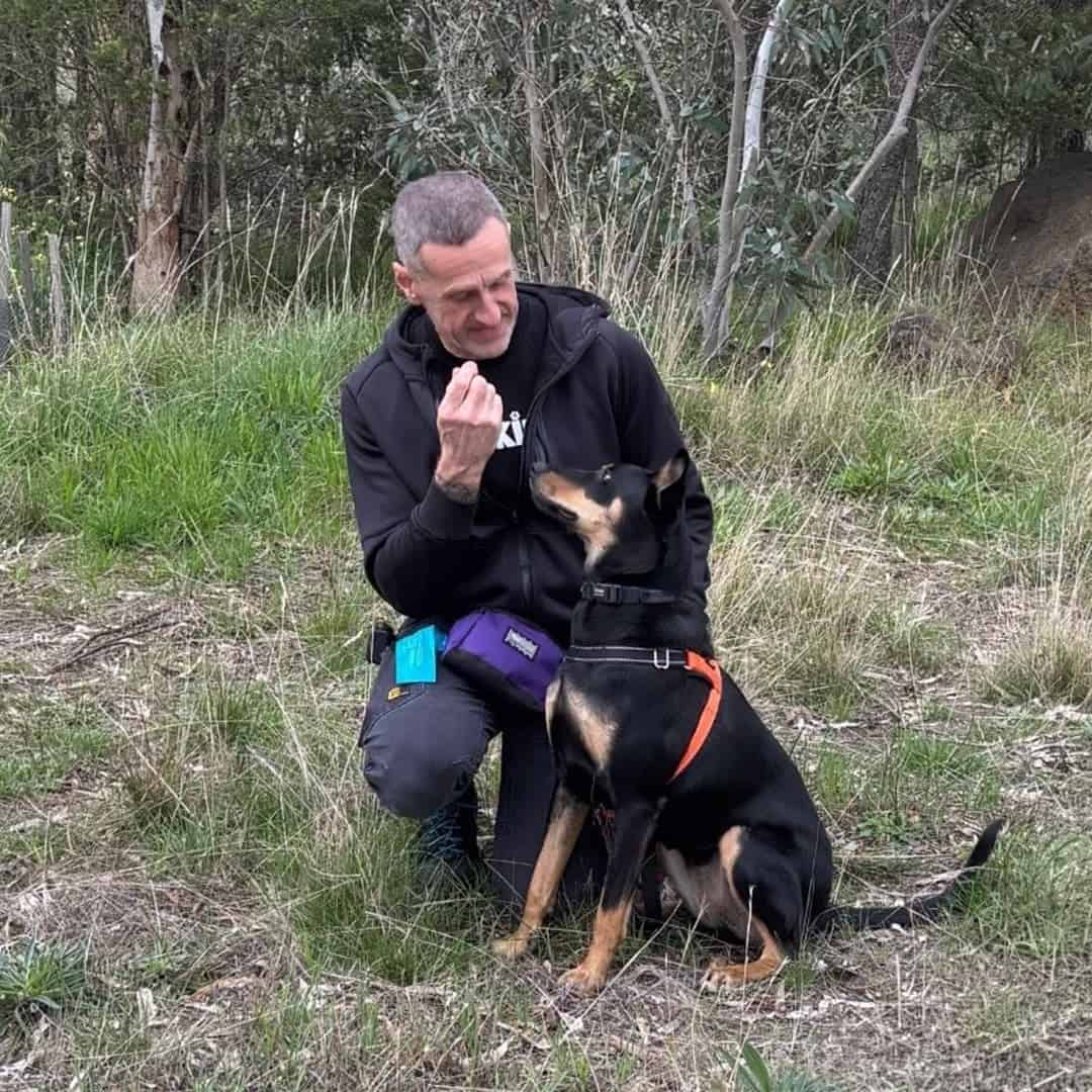 Gerry the trainer kneeling behind a black dog